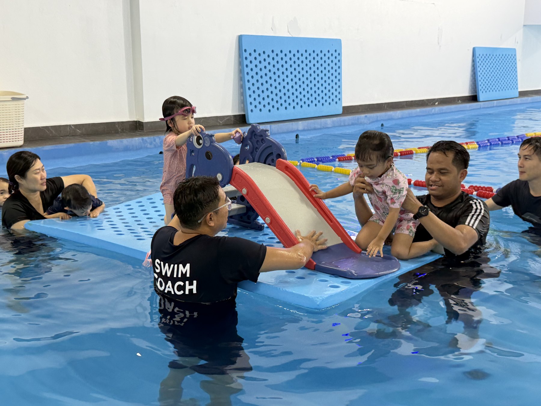 Skywhale coaches playing with babies and toddlers on the pool slide