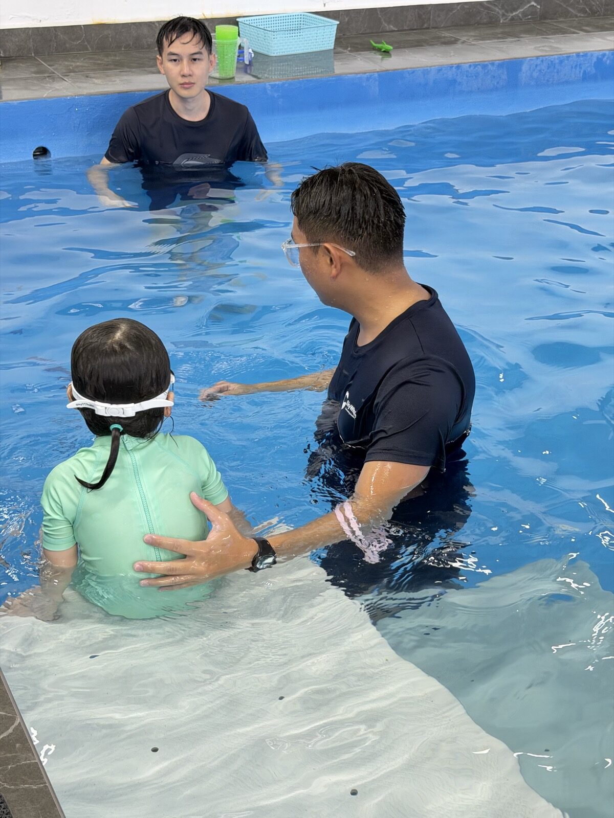 Kiddie swimming lesson — coach holding child in heated indoor pool, Puchong
